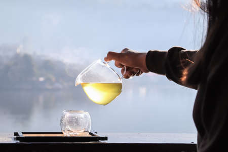 Female hands pouring hot tea with lake background at sunrise.の写真素材
