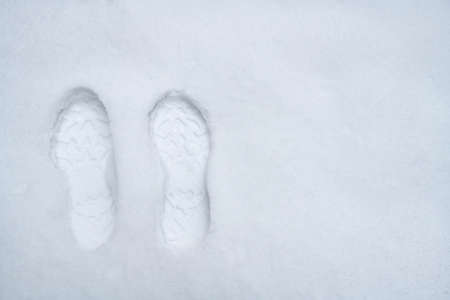 Footprints of one pair of shoes standing on snow with space for writingの写真素材