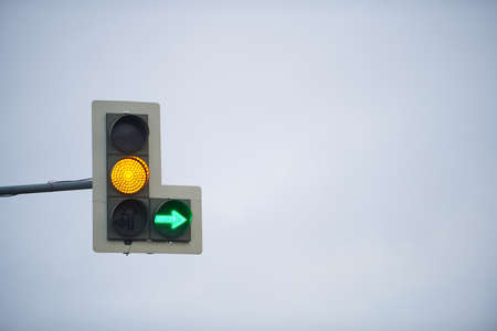 Traffic light with yellow light and green arrow on the background of cloudy skyの写真素材