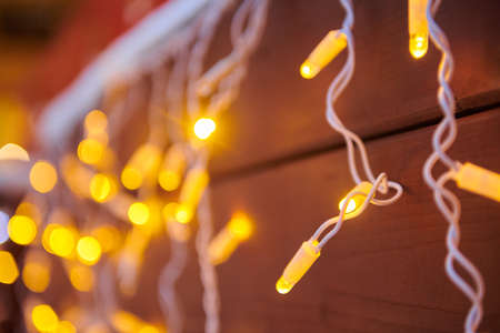 Christmas decorative yellow lights on the background of wooden wall, close-up
