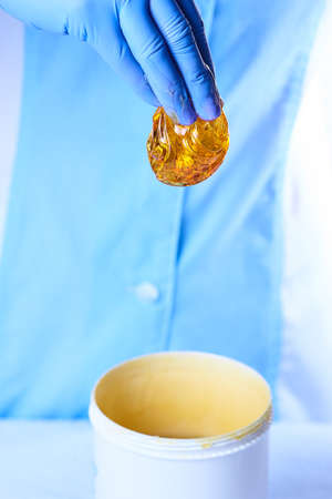 A new pack of sugaring paste and a piece of golden luminous sugaring paste in a hand