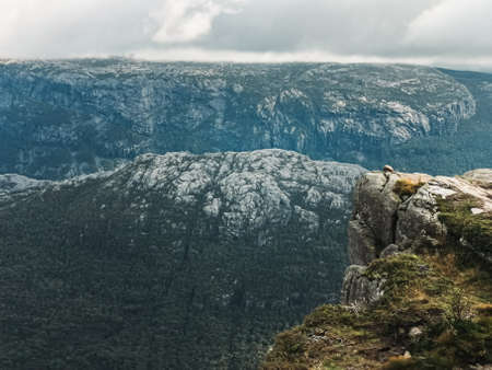 A vertical shot of a person sitting on top of a rock in the mountainsの写真素材
