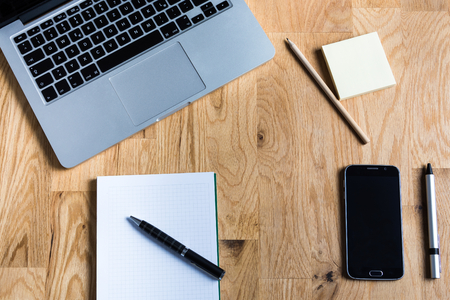Work environment with a laptop, smartphone, notepad and other accessories on wooden table from aboveの写真素材