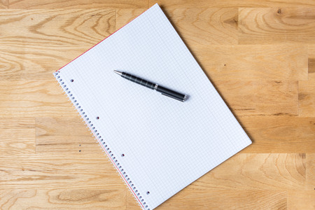 Work desk with note pad and biro on wooden table from aboveの写真素材