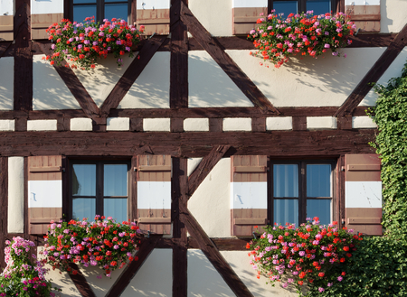 Half-timbered house with several window shutters and colorful flowersの写真素材
