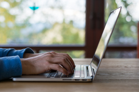 Typing on a laptop in front of window on wooden table