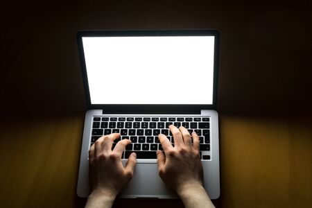Man working on laptop with white screen glowing in the dark from above