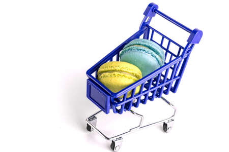 Blue and yellow macarons and metal shopping cart isolated on white backgroundの写真素材