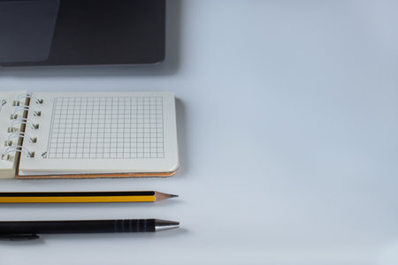 Office desk with spiral notepad, pencil and laptop on white backgroundの写真素材