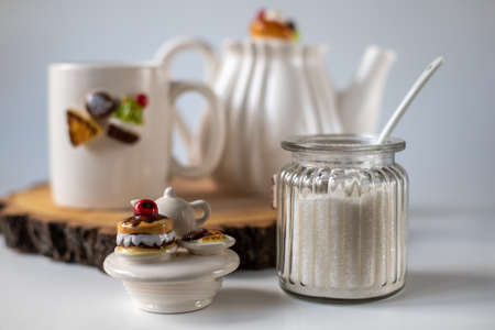 Sugar in a transparent jar. White utensils for tea drinking. The decor on the dishes is sweets. Cup, sugar bowl and teapot. Good morning. Screensaver wallpaperの写真素材