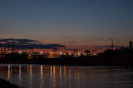 Dam at night. Concrete dam on the river. Night city with lights at beautiful sunset Long exposure view dam and city on sunset, vivid, blurry. Beautiful industrial landscapeの写真素材