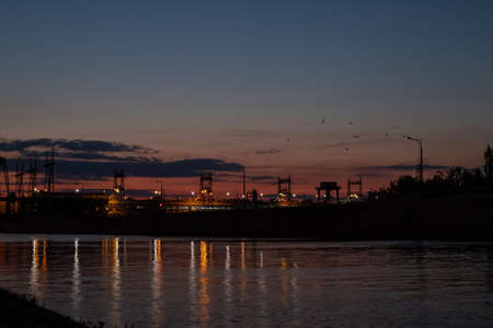 Dam at night. Concrete dam on the river. Night city with lights at beautiful sunset Long exposure view dam and city on sunset, vivid, blurry. Beautiful industrial landscapeの写真素材