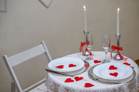 Table with white tablecloth. Romantic candlelight dinner. White fireplace decorated with red hearts for Valentines Dayの写真素材