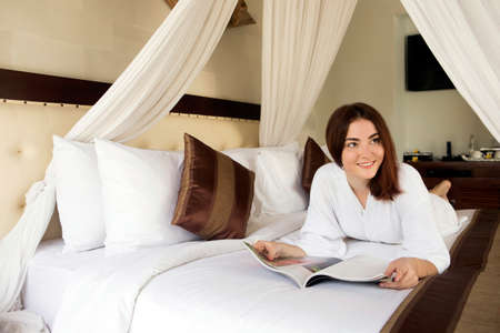 The girl smiles keeping magazine lying on a bed.の写真素材