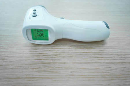 Non-contact infrared thermometer is the wooden table. On the green screen the figure numeral is 36.6の写真素材