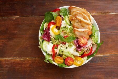 Healthy lunch salad with tomatoes, chicken, bell peppers, radishes and mozarella cheese on wooden background.の写真素材