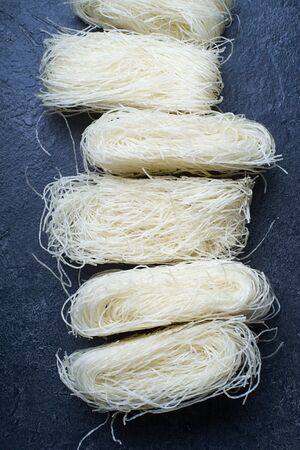 Uncooked rice noodles rolled in nests on dark background. Ingredient of asian cuisine.の写真素材