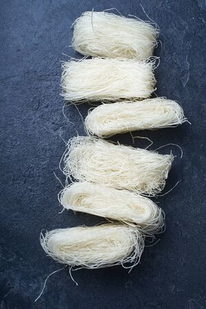 Uncooked rice noodles rolled in nests on dark background. Ingredient of asian cuisine.の写真素材