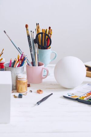 Interior of painting studio of freelance artist. Gypsum shapes, brushes, pencills, ink and paint bottles with sketchbooks on the table. Freelance artist lifestyle concept. Copy spaceの写真素材