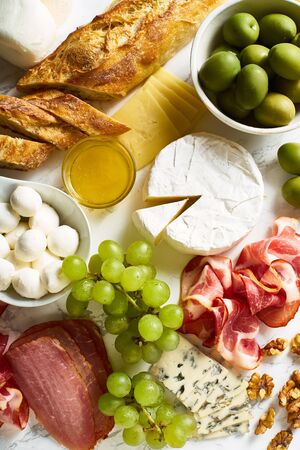 Cheese plate with brie, parmesan, cheddar and meat. Flatlay with variety of gourmet snacks, fruits and baguette on marble board.の写真素材