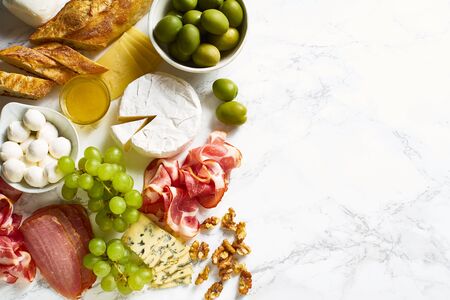 Cheese plate with brie, parmesan, cheddar and meat. Flatlay with variety of gourmet snacks, fruits and baguette on marble board. Copy spaceの写真素材
