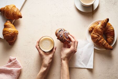 Flatlay with coffee and croissants. Female hand holding a cup of capuccino. Breakfast beverage with pastry. Morning setの写真素材