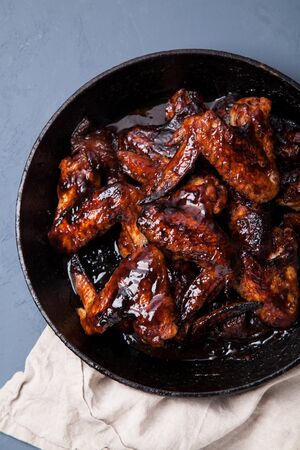 Chicken wings in thick barbecue sauce with garlic on black cast iron pan on gray rustic background. の写真素材
