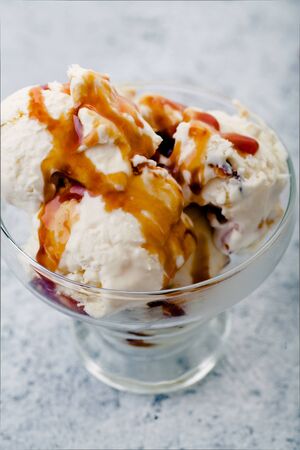 Caramel ice cream scooped in glass bowl from metallic container. Peanuts and chocolate used for...