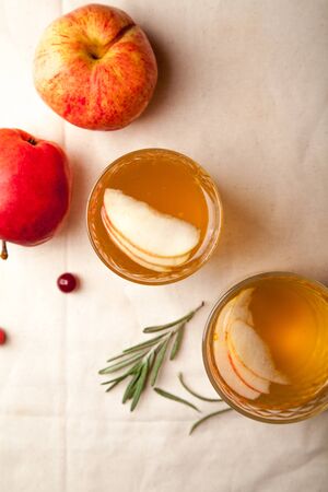 Two vintage glasses with apple cider on black background. Christmas beverages concept. Two red apples and rosemary sprig aside.  Warm backlight. Vertical composition. Top view.の写真素材