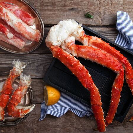 Fresh crab claws and different types of crab meat on black wooden tray on vintage wooden background with vintage plates and lemon slices. Square.の写真素材