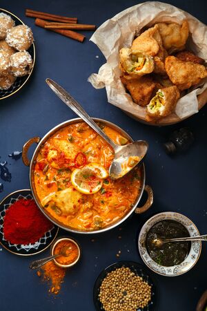 Indian cuisine on diwali holiday: tikka masala, samosa, patties and sweets with mint chutney and spices. Dark blue background. Vertical compositionの写真素材