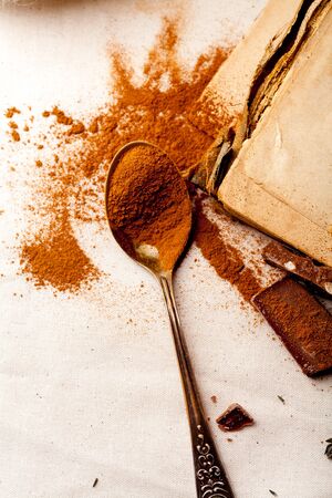 Tea spoon with spilled cocoa powder on linen background with old-fashioned cookbooks aside. Top view. Vintage kitchen concept. Macro view.の写真素材