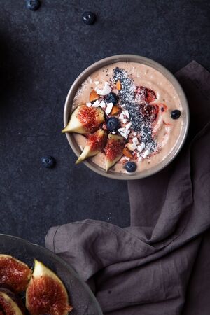 Blueberry banana smoothie bowl with figs and coconut. Dark food photography concept. Flatlay with copy spaceの写真素材