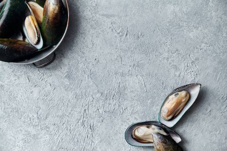 Overhead view of raw kiwi mussels in copper plate on textured light colored background with text...