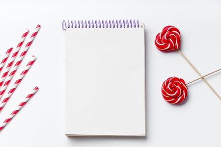Red and white party drinking straws with lollipops and empty notebook on white background with copy spaceの写真素材