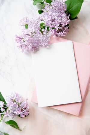Top vew composition with feminine workspace mock up with empty card, lilac flowers and pink notebook on marble backgroundの写真素材