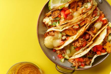 Close up of mexican tacos with chili con carnes and grated cheese served over a yellow background...