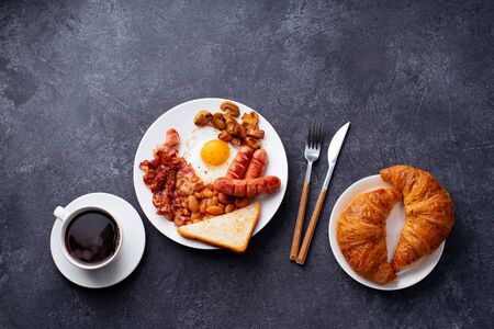 Classical english breakfast with fried bacon, mushrooms and eggs. Served with croissants and black coffee.の写真素材