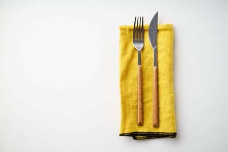 Knife and fork on yellow textile napkin on white background with copy spaceの写真素材