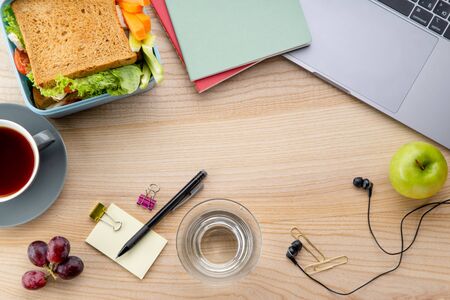 Overhead image of healthy sandwich in plastic container with some fruits on wooden table next to opened laptop. Daily office or school lunch conceptの写真素材