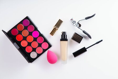 Overhead image of makeup products: lipstick  palettes, foundation, mascara and eyelash curler on white background. Make-up artist kit conceptの写真素材