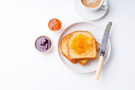 Morning toasts with butter and confiture on white table served with a cup of coffee with milk. Top view, flatlayの写真素材