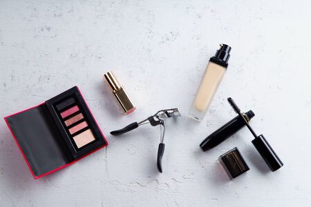 Top view picture of makeup products: lipstick, glossy eyeshadows, foundation, mascara and eyelash curler on textured stone background. Make-up artist kit conceptの写真素材