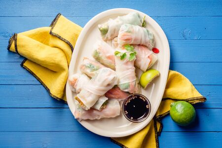 Vegetarian spring rolls with tofu, marinated carrot and daikon and cilantro on blue painted wooden table with yellow textileの写真素材