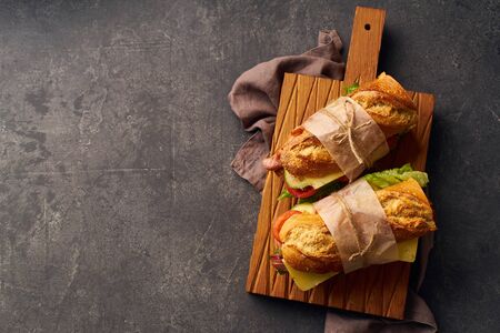 Fresh big baguette sandwich with bacon, chedder cheese, mustard, lettuce and vegetables on dark background                            の写真素材