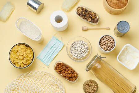 Top view of food staples prepared to survive Coronavirus COVID 19 pandemic at the time of cuarentine and home isolation. Pasta, chickpeas, nuts, cans and toilet paper. Flatlay on yellow backgroundの写真素材