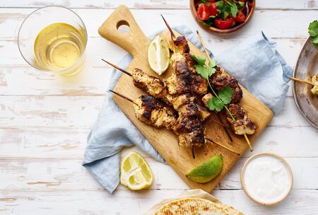 Chicken tikka kebab with red onion, coriander and fresh salad. Traditional indian dish made of chicken marinated in yoghurt and spices. Creative flatlay on white wooden background.の写真素材