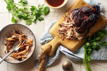 Top view of slow roasted glazed pork with barbecue sauce and herbs on wooden cutting boardの写真素材