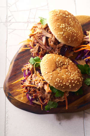 Pulled pork burgers with pickled and fresh vegetables and coriander on white tiled background