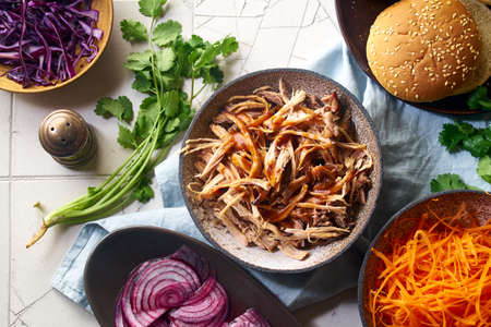 Flat lay with shredded pulled pork, barbecue sauce, pickled vegetables and buns. Cooking burger with slow roasted porkの写真素材